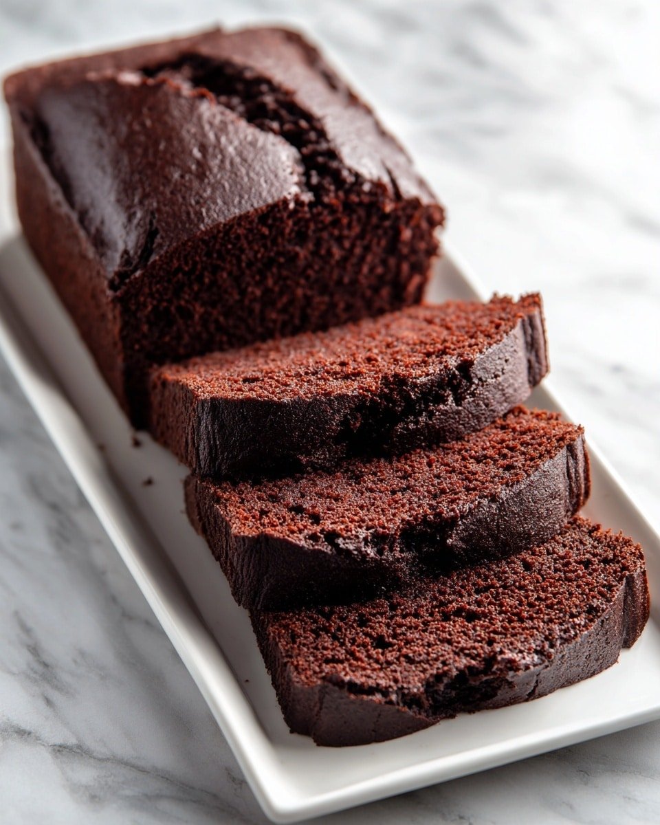 A loaf of dark chocolate cake is placed on a long white rectangular plate sitting on a white marbled surface. The cake has a smooth, slightly shiny top crust and a dense, moist texture inside. Four thick slices are cut and slightly fanned out in front of the rest of the whole loaf, showcasing the rich, dark brown color and soft crumb of the cake. The warm tone of the cake contrasts with the clean white plate and marble background. Photo taken with an iphone --ar 4:5 --v 7 — Gingerbread Loaf, cozy gingerbread loaf recipe, holiday gingerbread cake, spicy gingerbread bread, easy gingerbread loaf